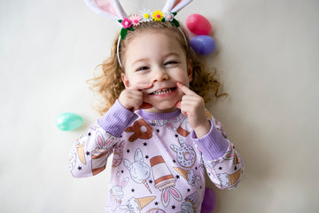 Little girl wearing cute easter sleepwear for kids, girl Easter pajamas with bunny shaped sweet treats on a lavender stretchy background. 