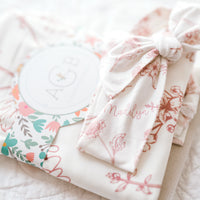 A white cloth with a floral pattern and a bow tied around it, along with a small circular tag that says "AGB".