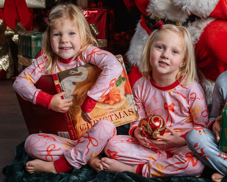 Little girl wearing pink personalized christmas pajamas with red pink and orange bows, and her name in red letters scattered around with red cuffs