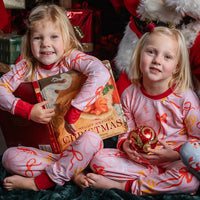Little girl wearing pink personalized christmas pajamas with red pink and orange bows, and her name in red letters scattered around with red cuffs