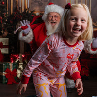 Little girl wearing pink personalized christmas pajamas with red pink and orange bows, and her name in red letters scattered around with red cuffs