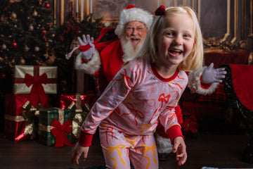 Little girl wearing pink personalized christmas pajamas with red pink and orange bows, and her name in red letters scattered around with red cuffs