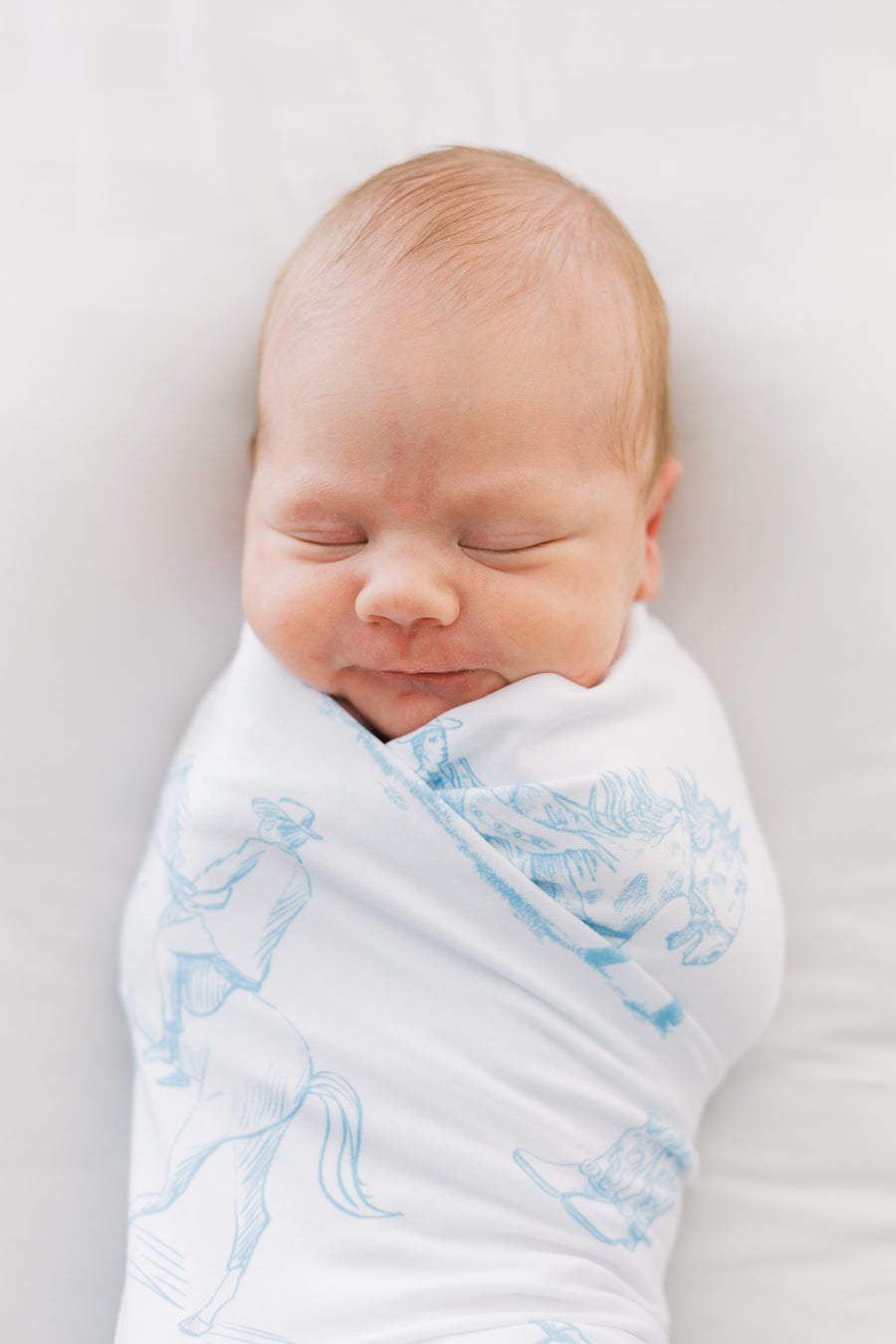 baby boy swaddled in blue western toile print white knit baby blanket with name