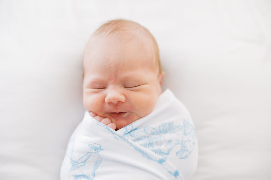 baby boy swaddled in blue western toile print white knit baby blanket with name