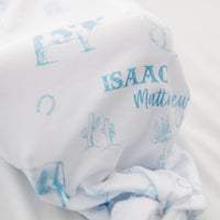 baby boy in tie bottom baby gown with light blue western toile print personalized with name and matching knotted hat