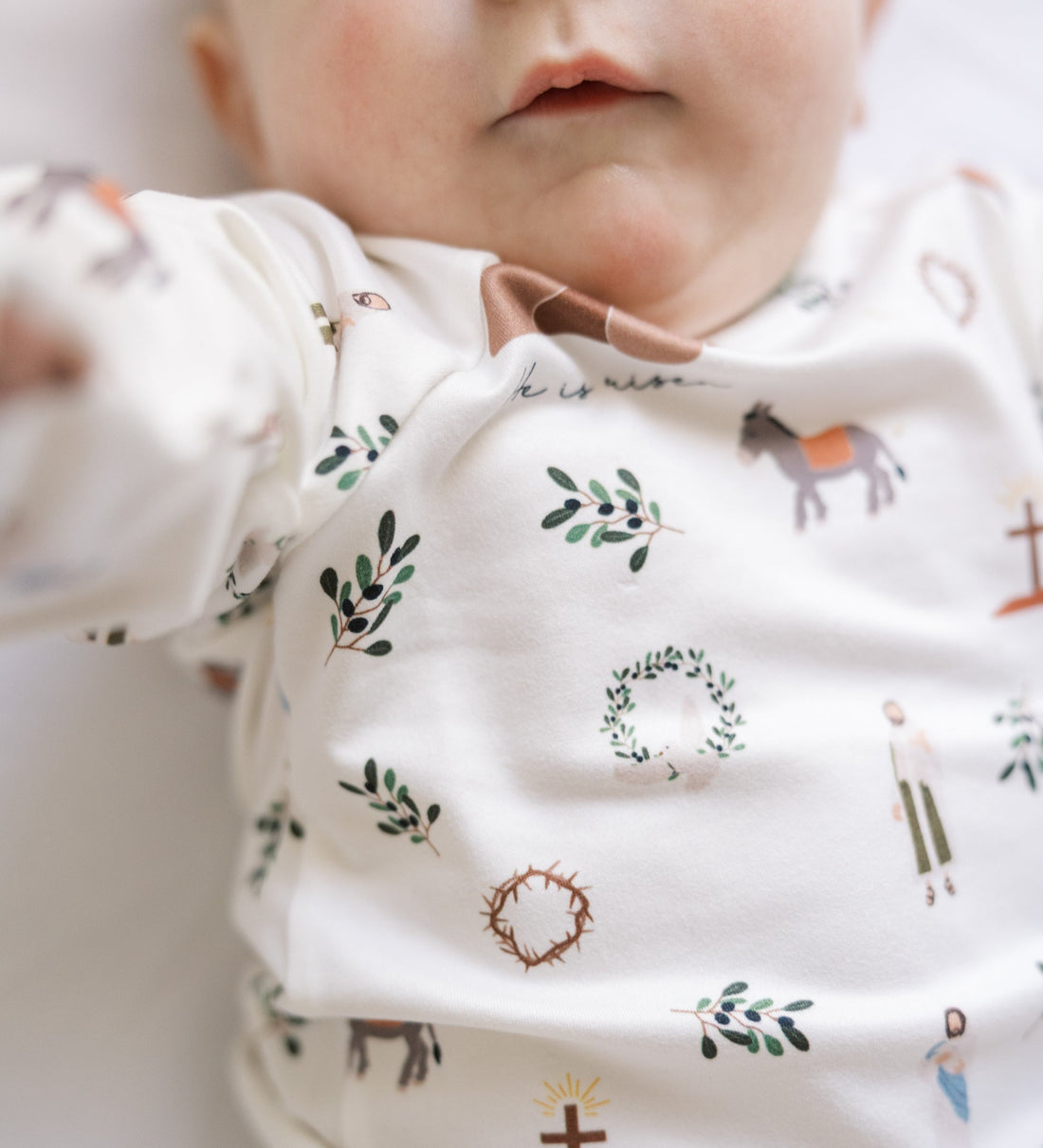 baby wearing personalized He is Risen Easter PJs with Biblical Easter images on a white stretchy knit fabric, perfect for babies toddlers and big kids.