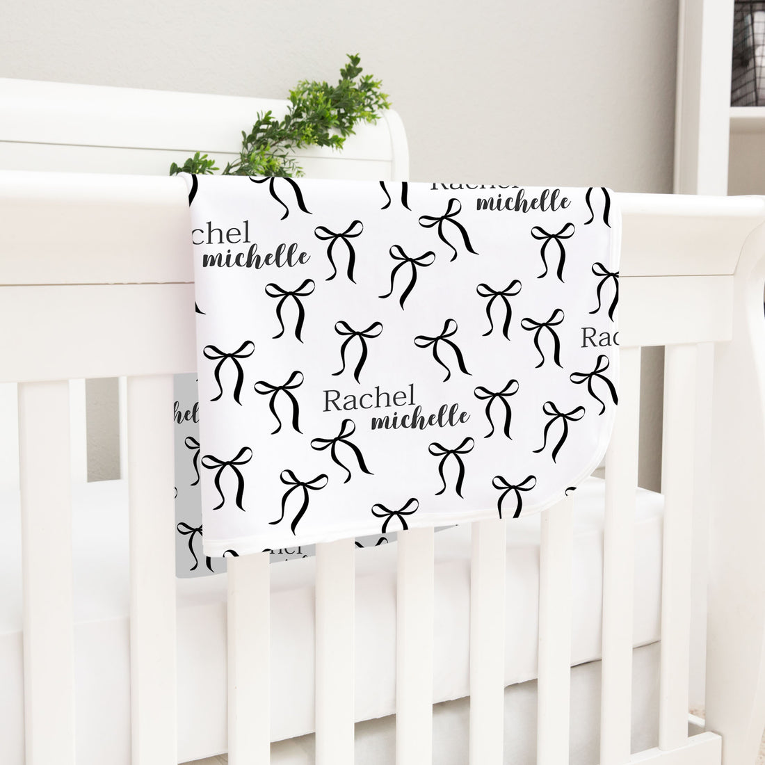 A white crib with a black and white patterned blanket featuring the name "Rachel" and the name " Michelle" printed on it.