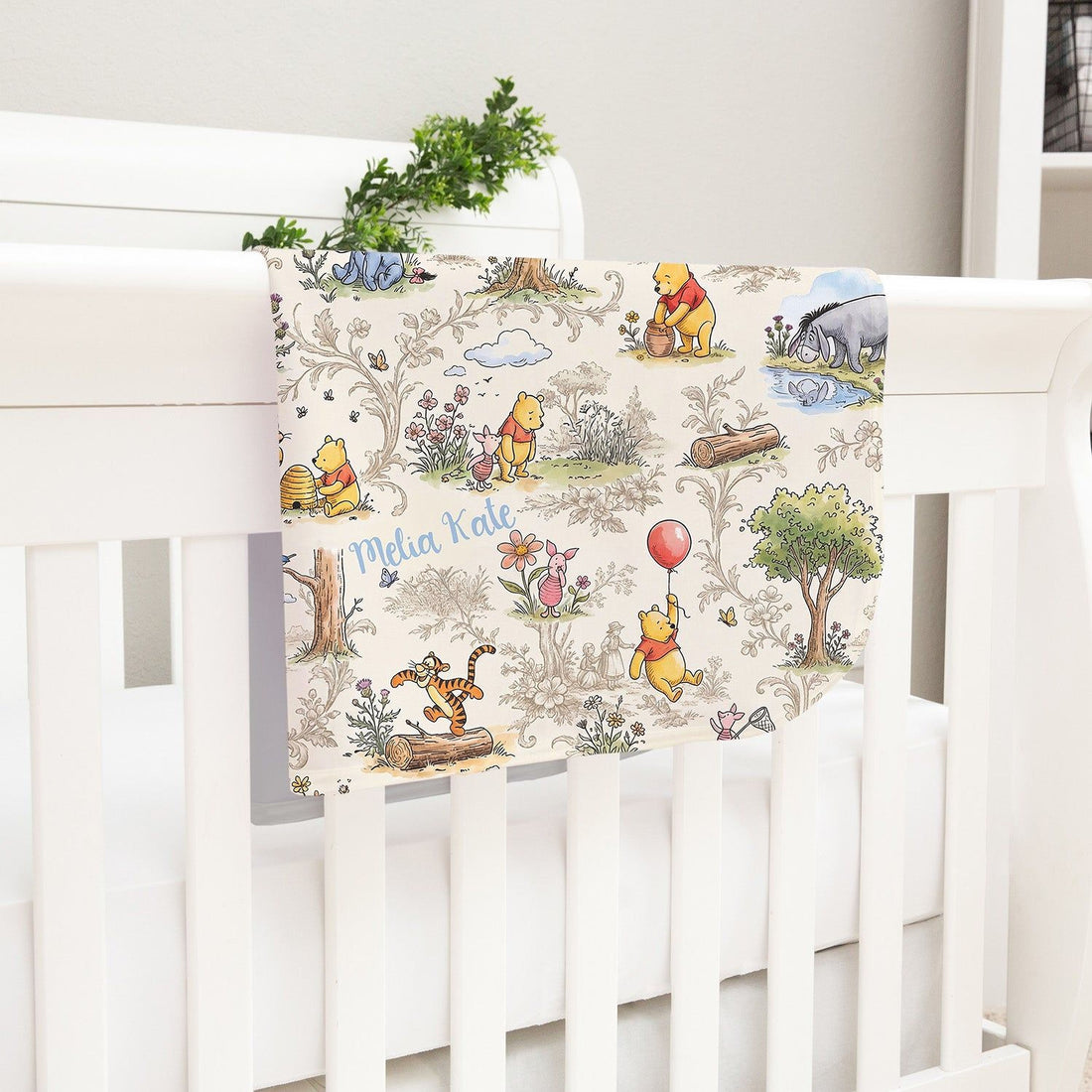 A white crib with a Winnie the Pooh-themed blanket hanging on the side.