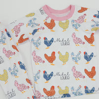 personalized chicken pajamas with a  calico design in various colors, her name in script font on a white knit background, and pink cuffs. 