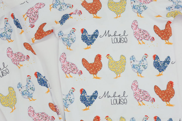 personalized chicken pajamas with a  calico design in various colors, her name in script font on a white knit background, and pink cuffs. 