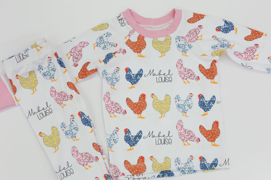 personalized chicken pajamas with a  calico design in various colors, her name in script font on a white knit background, and pink cuffs. 