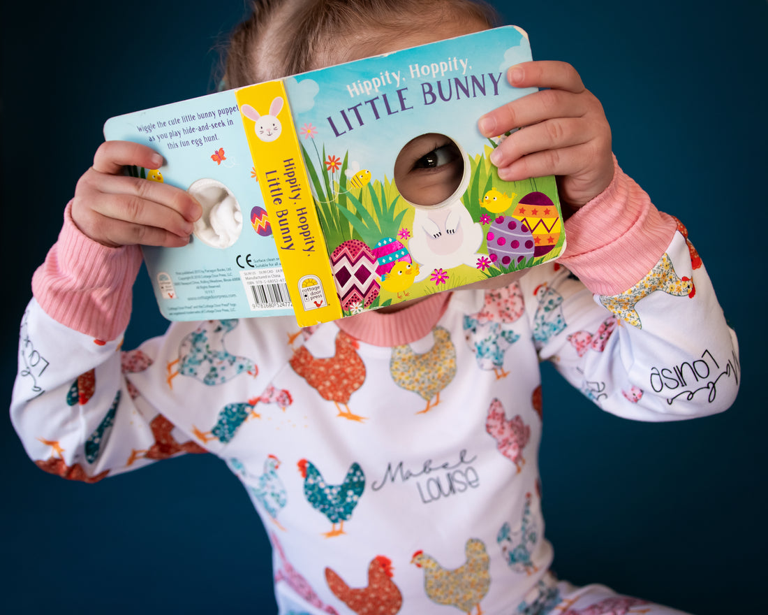 Child reading a book and being playful while she is wearing her personalized chicken pajamas. 