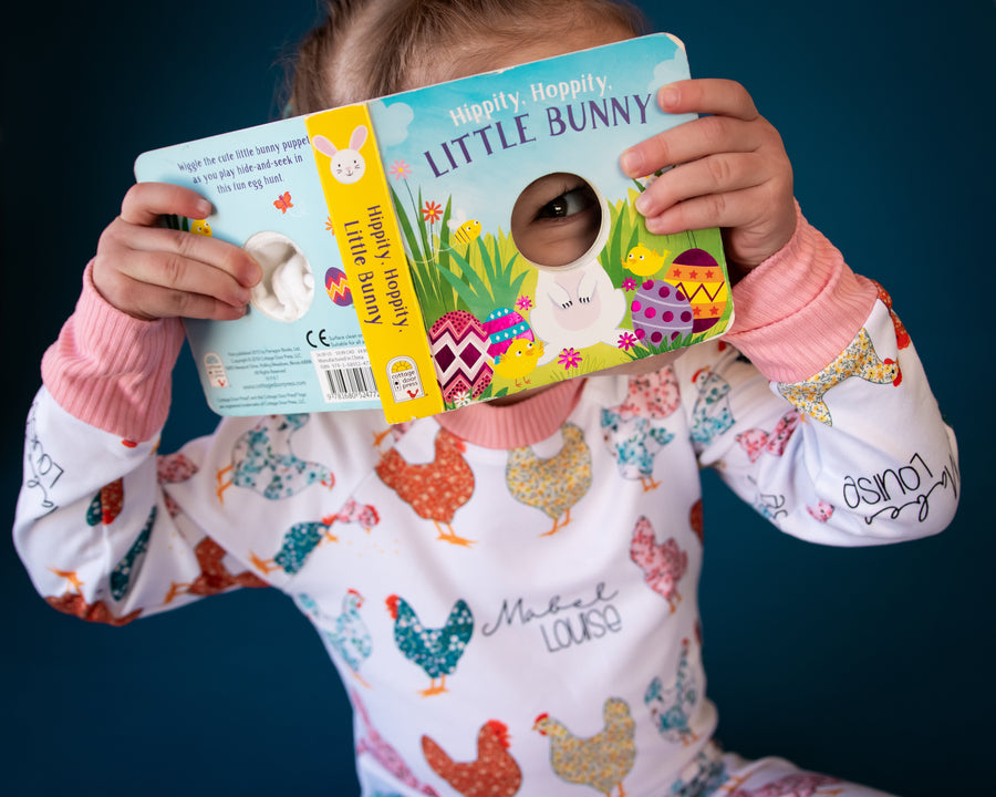 Child reading a book and being playful while she is wearing her personalized chicken pajamas. 