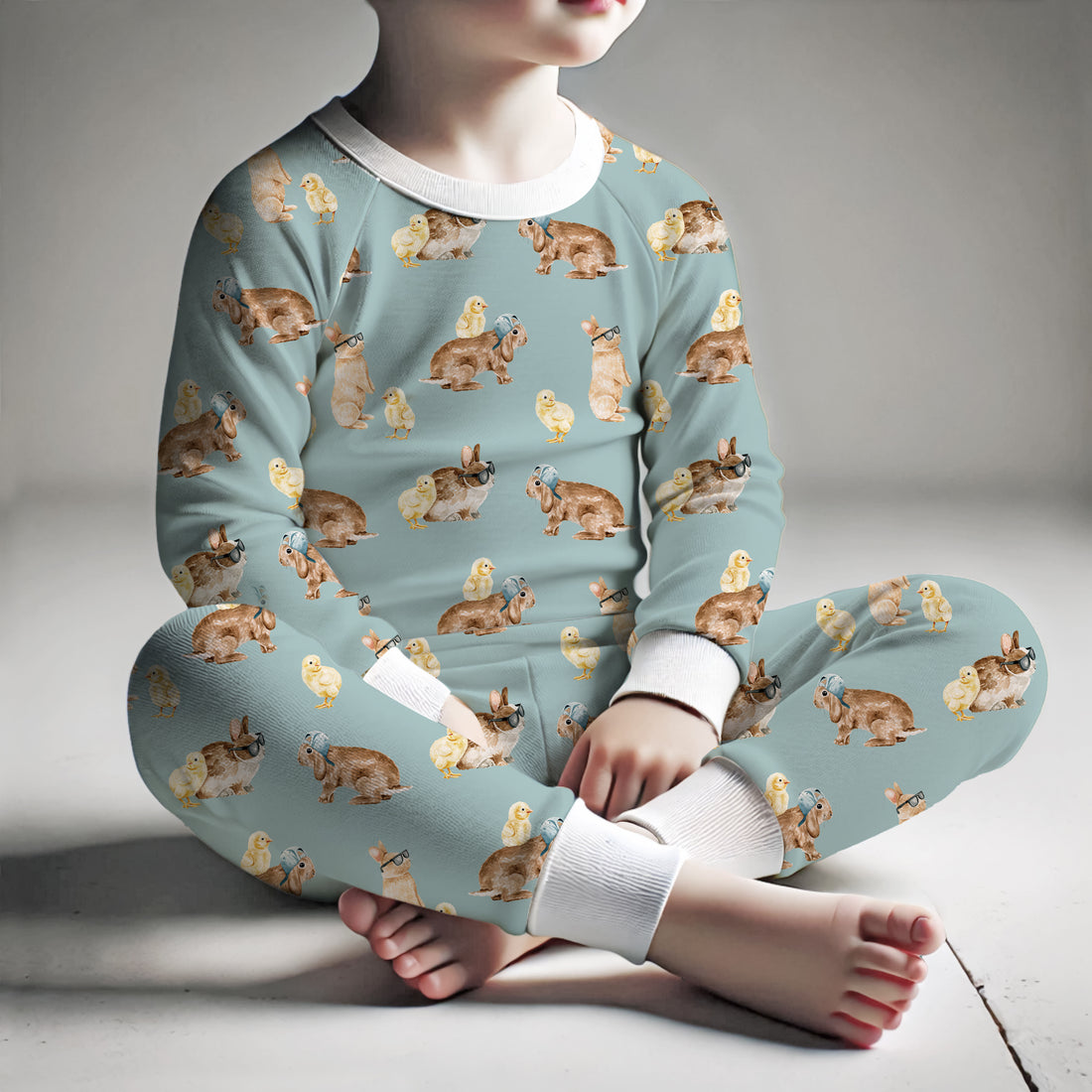 little boy wearing kid's Easter bunny pajamas with chicks and rabbits on a teal background.