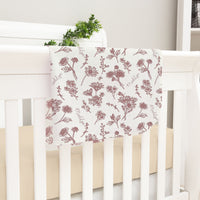 a white crib with a floral print blanket hanging on it.