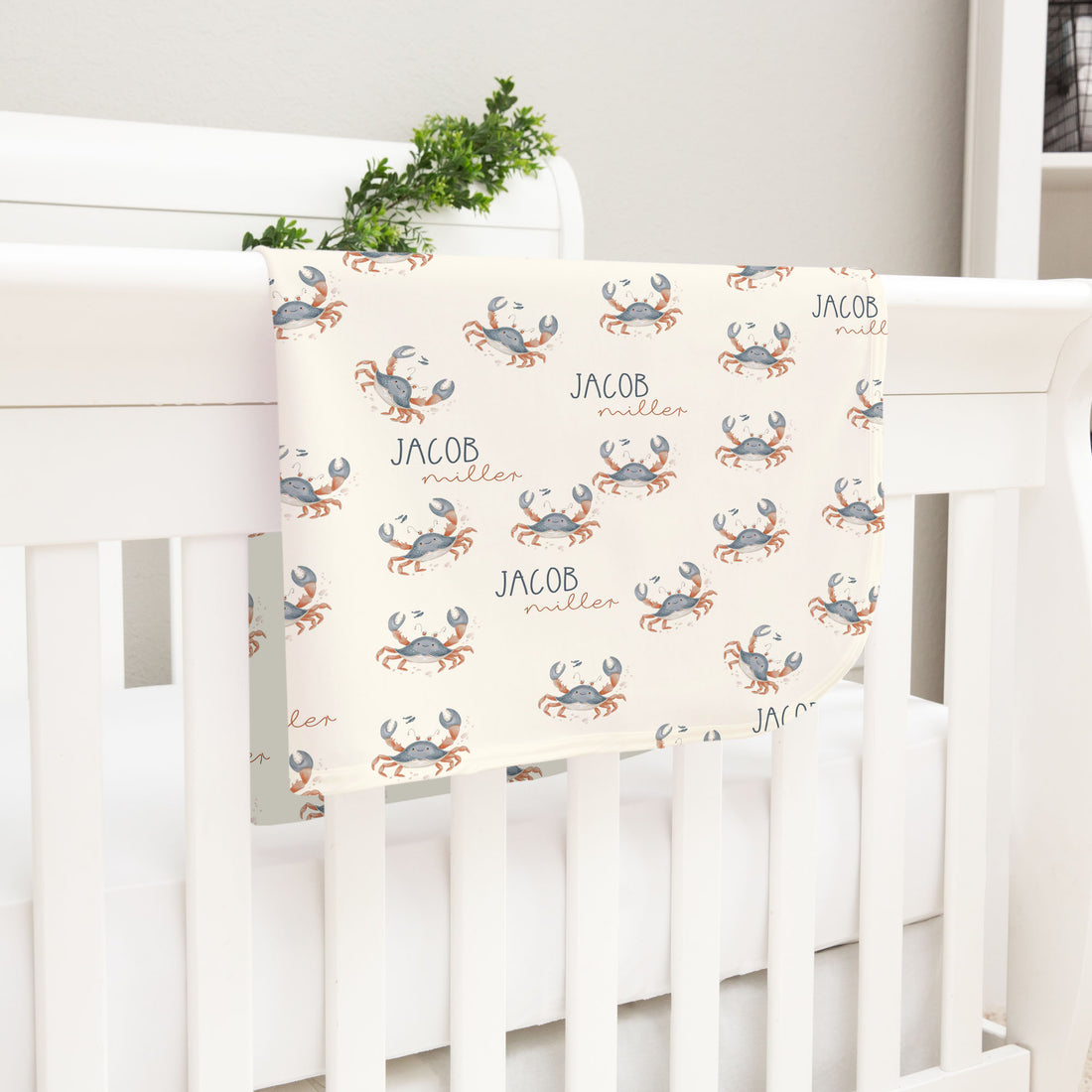 A white crib with a blanket featuring a repeating pattern of crabs.