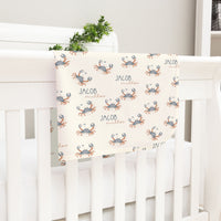 A white crib with a blanket featuring a repeating pattern of crabs.