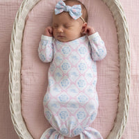 A newborn baby girl is peacefully sleeping in a white wicker basket, wearing a pink and white patterned onesie and a blue bow.