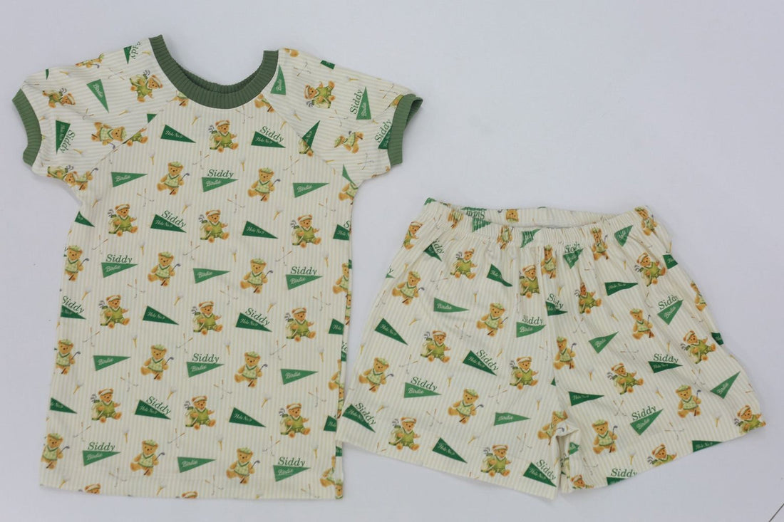 A white t-shirt and shorts with a repeating pattern of green and yellow teddy bear designs.