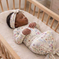 A newborn baby girl is peacefully sleeping in a wooden crib, wearing a white floral onesie and a matching headband.