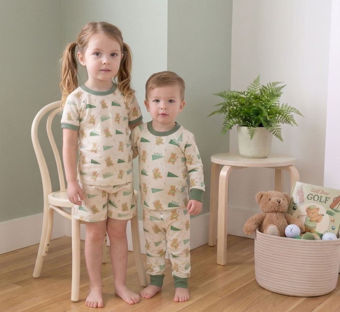 Two young children wearing pajamas with a bear pattern stand in a room with a chair, a potted plant, and a basket of toys.