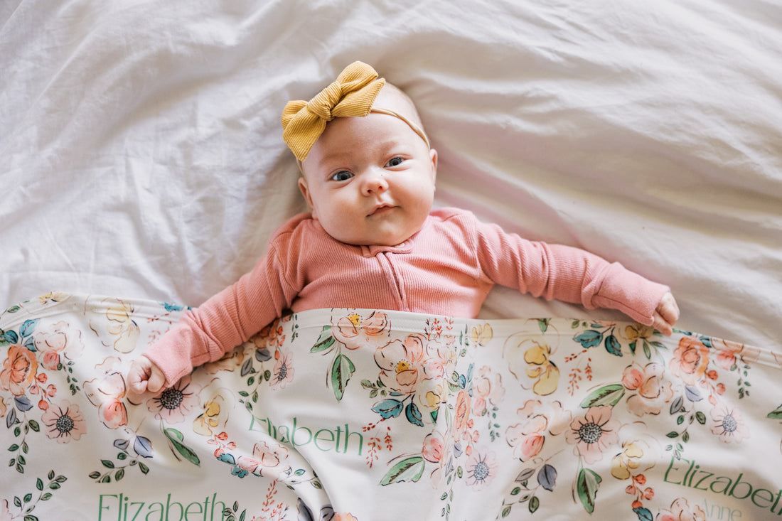 Baby lying on a floral blanket with a pink outfit and yellow headband.