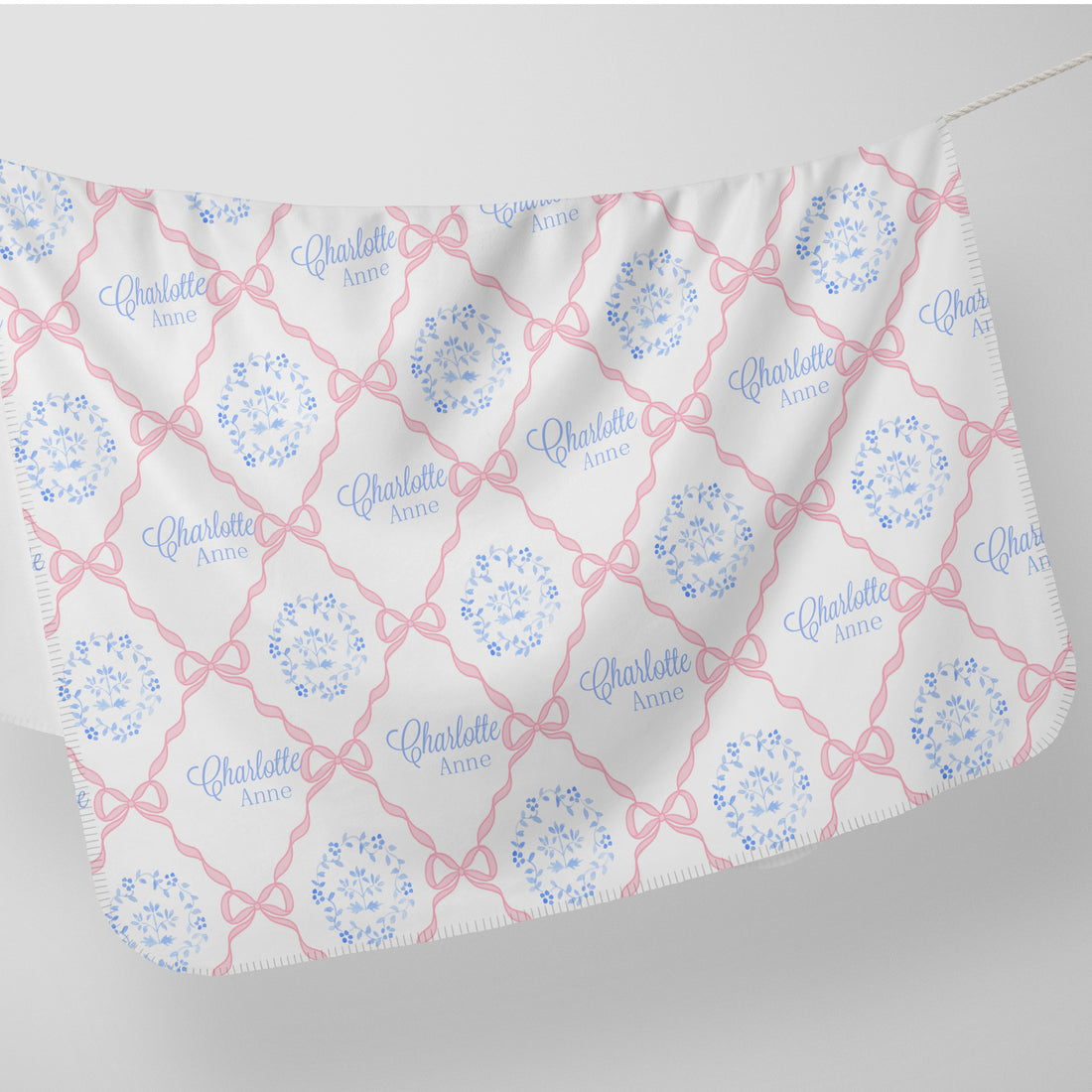 a white fabric with a repeating pattern of pink bows and the name "Charlotte" written in blue.