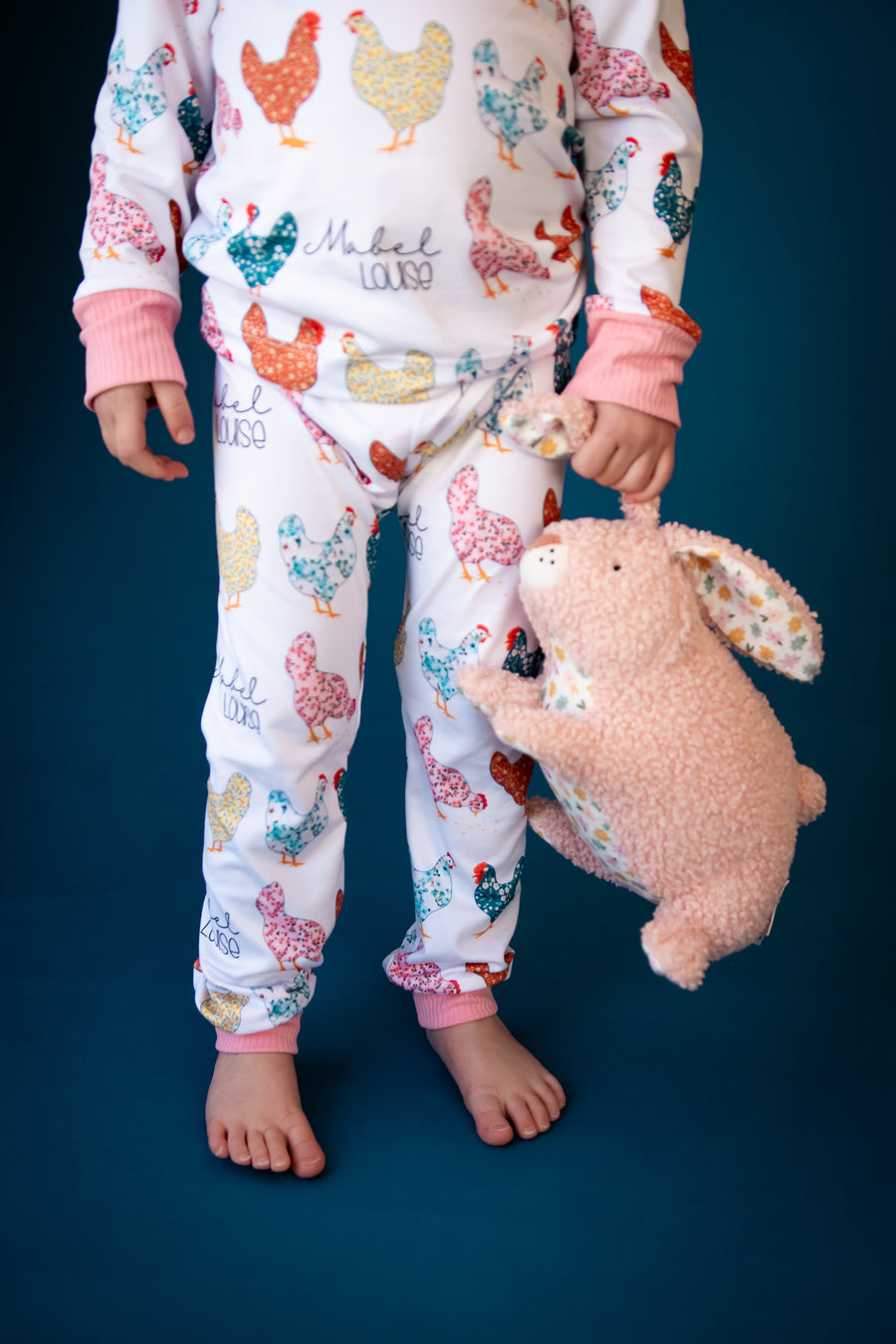 A child wearing her personalized chicken pajamas and holding her stuffed animal. 