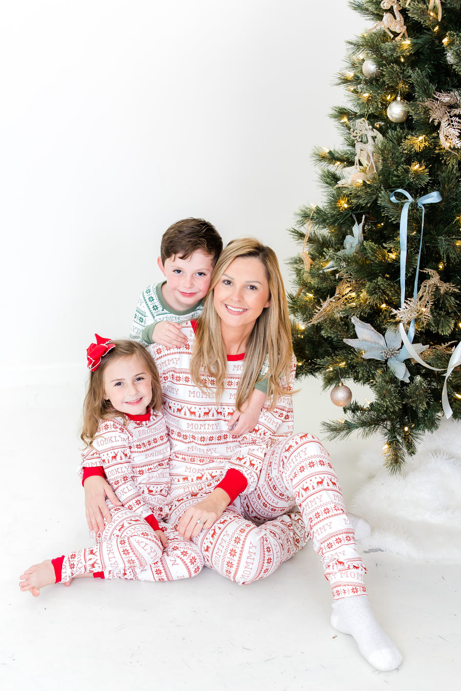 Mom and kids wearing matching striped Christmas pajamas in front of Christmas tree.