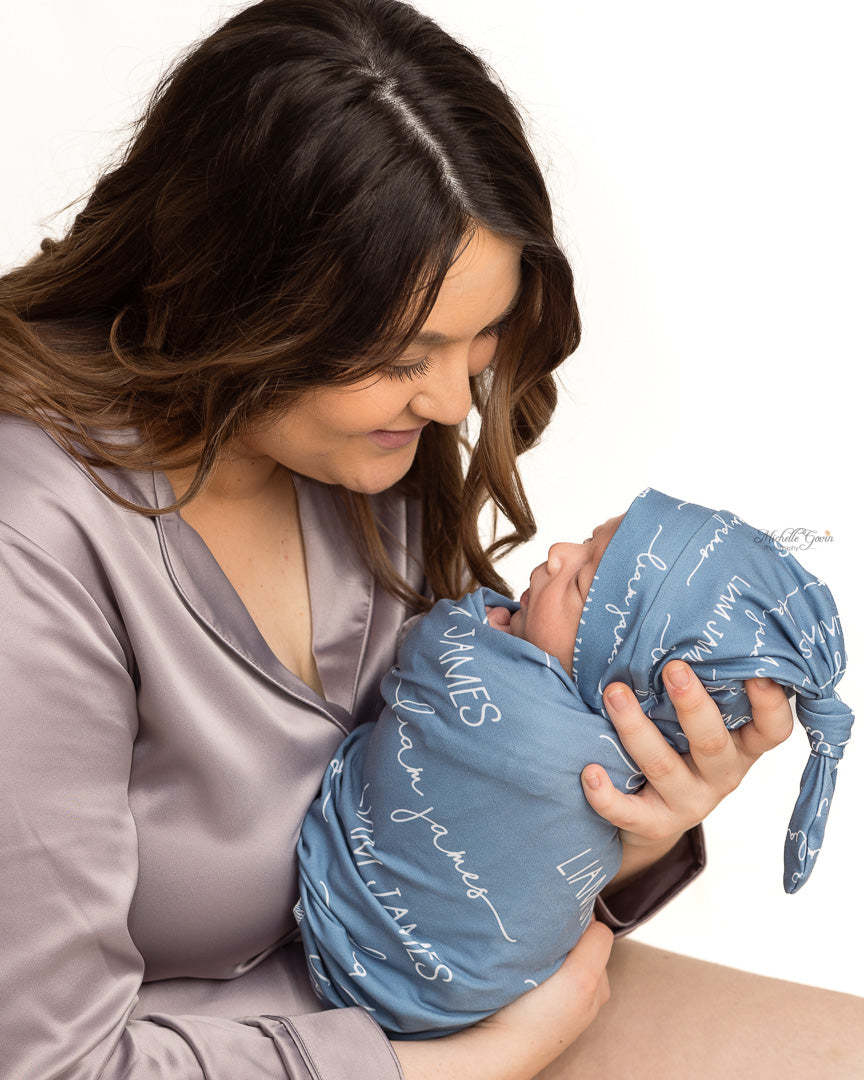 A mother holding her baby swaddled in their personalized camden stretchy swaddle blanket. 