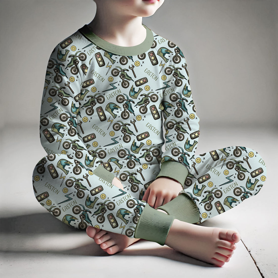 A young boy sitting in his personalized dirt bike pajamas. The dirt bike pajamas have long sleeves and long, cozy pants. 