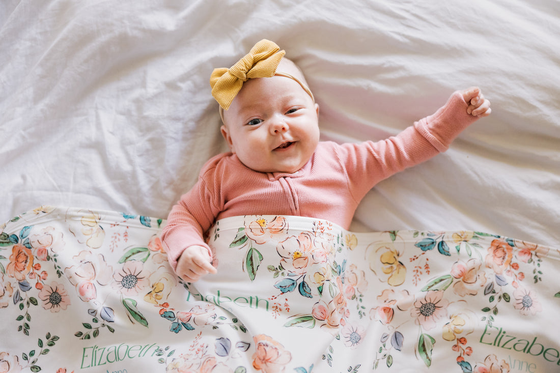 Baby lying on a floral blanket wearing a pink outfit and yellow headband.