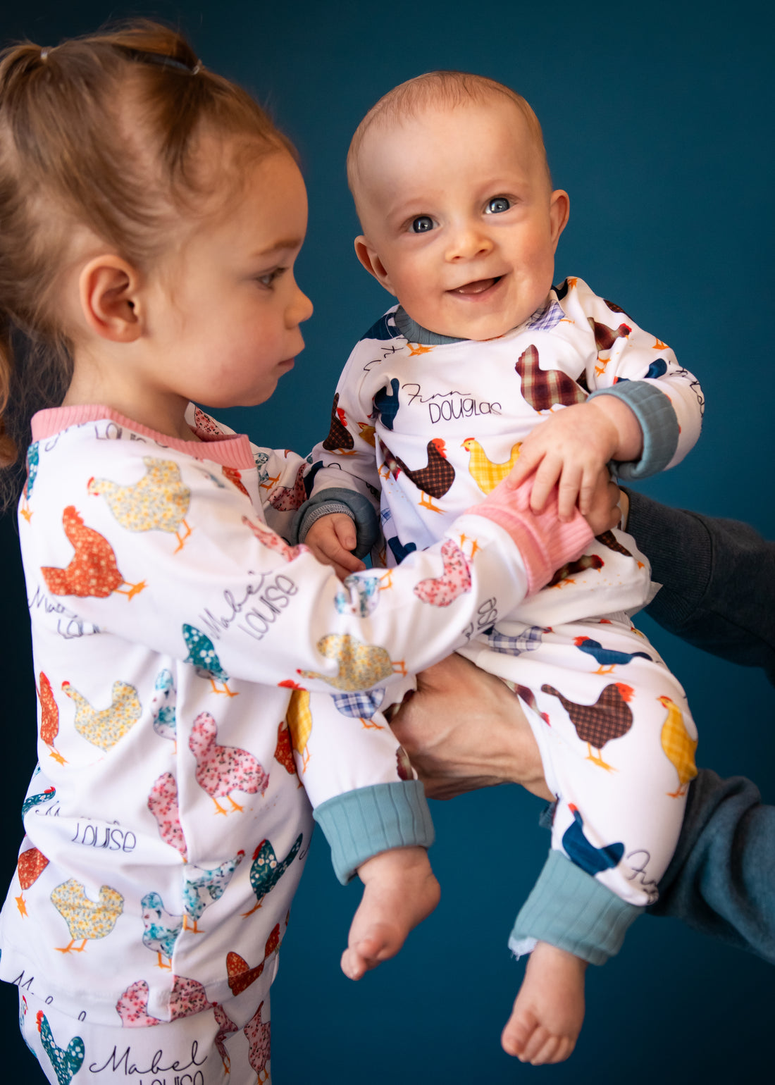 A young girl wearing chicken pajamas and holding her little brother who is also wearing matching chicken pajamas. 