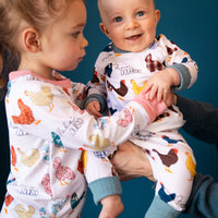 A young girl wearing chicken pajamas and holding her little brother who is also wearing matching chicken pajamas. 