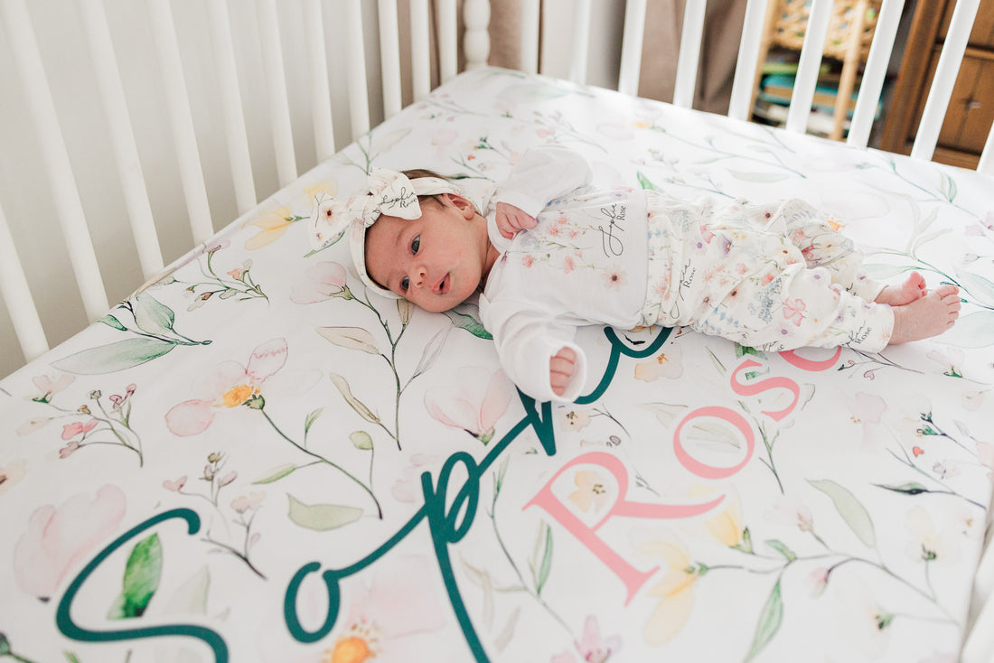 Baby girl on wildflower print personalized crib sheet, dainty wildflowers and baby's name on high-end luxury nursery bedding.