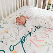 Baby girl on wildflower print personalized crib sheet, dainty wildflowers and baby's name on high-end luxury nursery bedding.