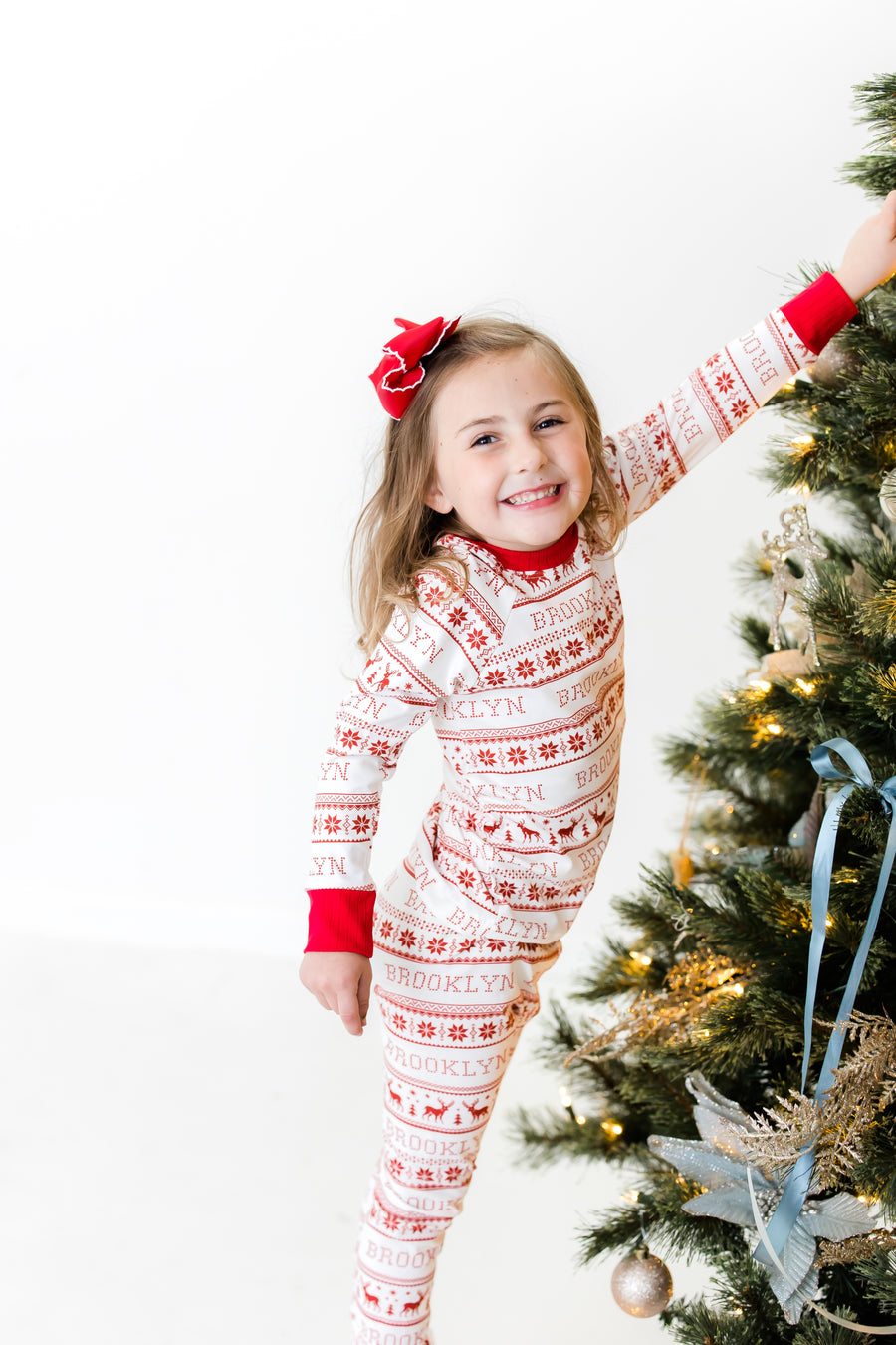 Young girl wearing red striped Christmas Pajamas and hanging ornaments on Christmas tree. 