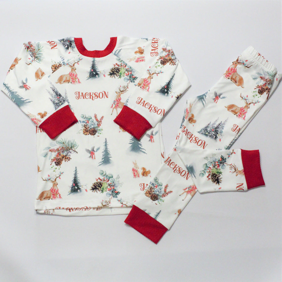 Christmas in the Forest soft and stretchy Christmas Pajamas with forest animals, trees, and pinecone bundles decorated for the holidays, on white fabric and red cuffs, with child's name scattered among the images.