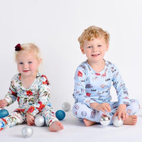 Baby girl wearing Floral Christmas Pajamas with bouquets of red, white, and light blue flowers and holly leaves, and sitting next to her brother in Christmas pajamas. 