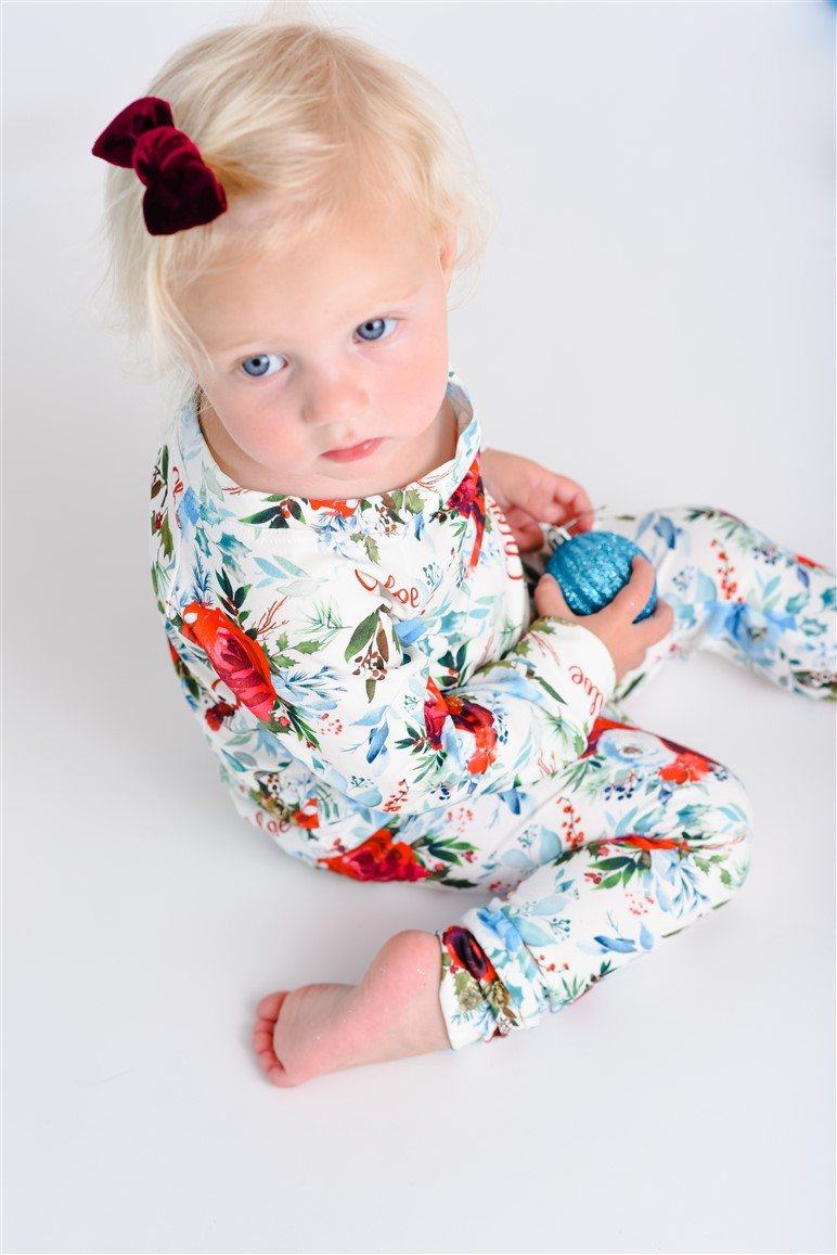 Young girl wearing Floral Christmas Pajamas with bouquets of light blue, white, and red flowers and holly leaves, and personalized with the child's name.