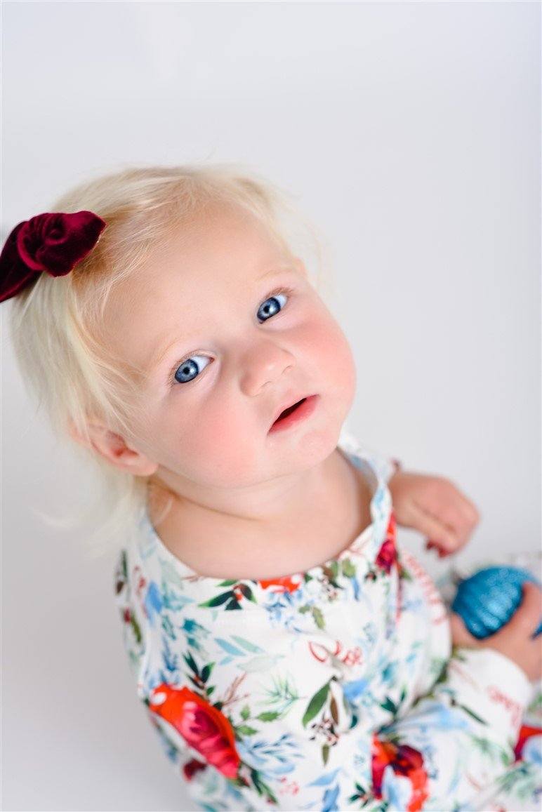 Young girl wearing Floral Christmas Pajamas with bouquets of red, white, and light blue flowers and holly leaves, and personalized with the child's name in red script font on a white background.