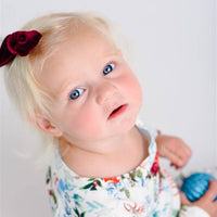 Young girl wearing Floral Christmas Pajamas with bouquets of red, white, and light blue flowers and holly leaves, and personalized with the child's name in red script font on a white background.