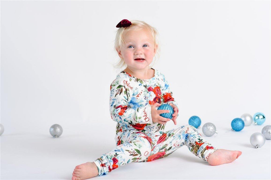 Little girl sitting and smiling while wearing floral Christmas pajamas with red, white and blue flowers. 