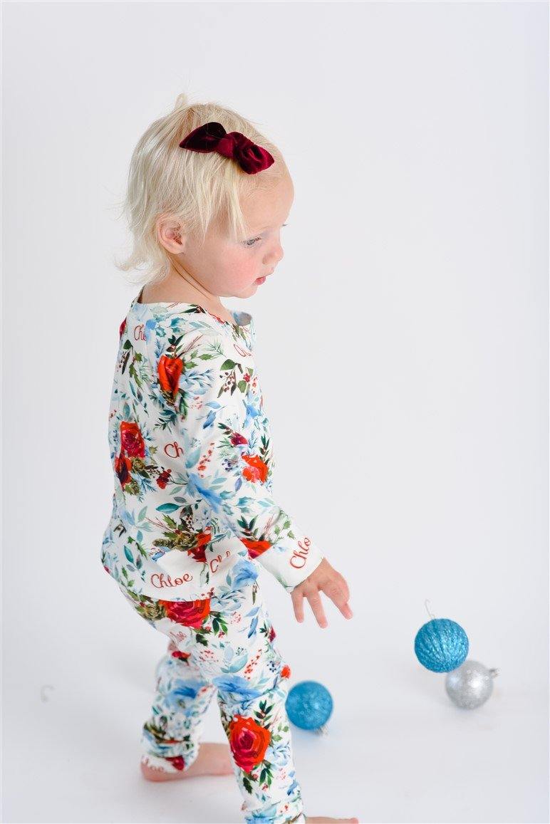 Young girl walking in flower Christmas Pajamas with bouquets of red, white, and light blue flowers and holly leaves.