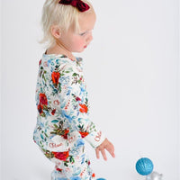 Young girl walking in flower Christmas Pajamas with bouquets of red, white, and light blue flowers and holly leaves.